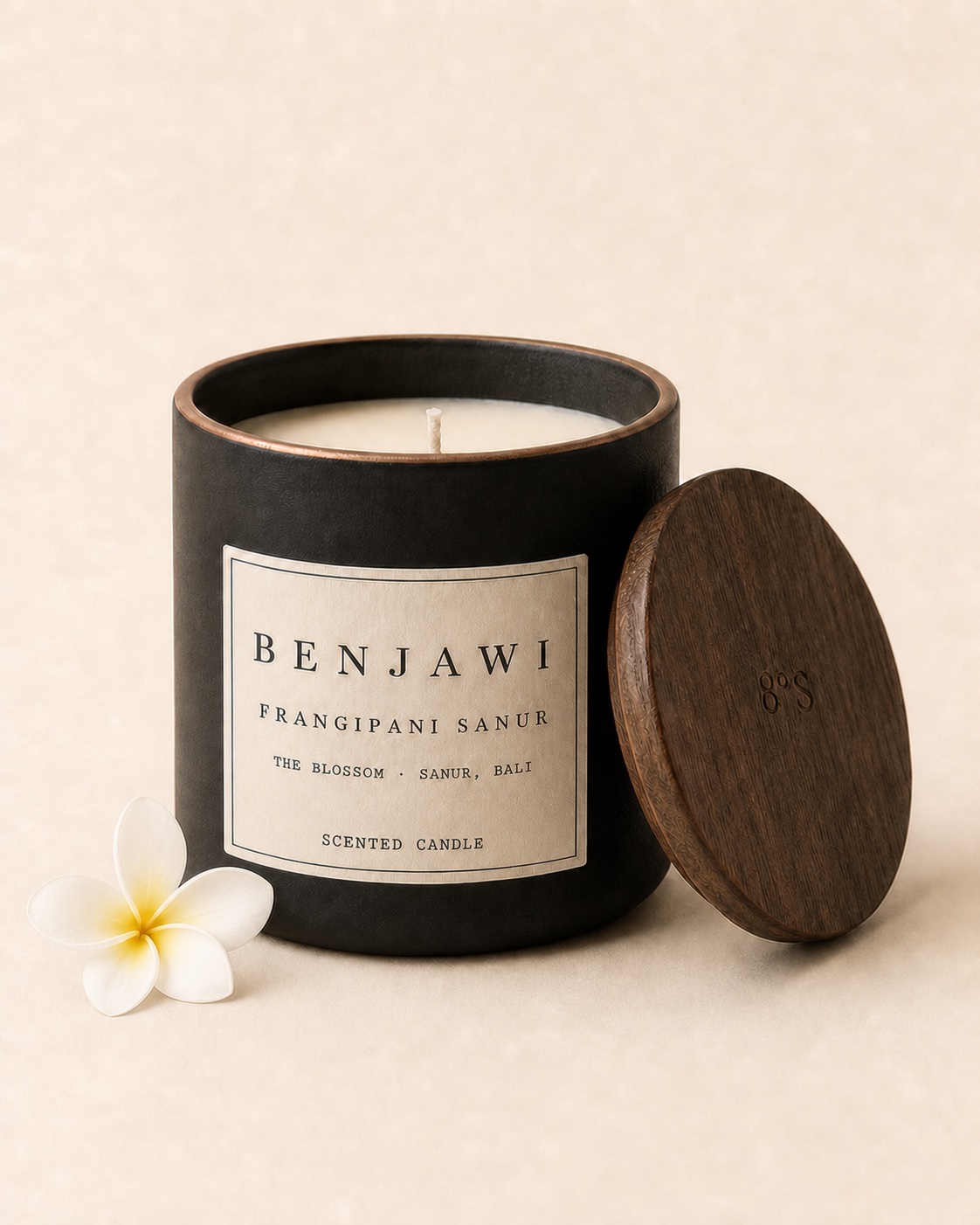 Benjawi Frangipani Sanur scented candle beside one white frangipani blossom